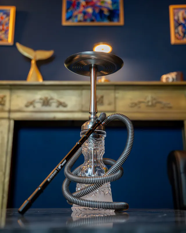 Shisha de acero con base de cristal tallado transparente, delante de la chimenea dorada