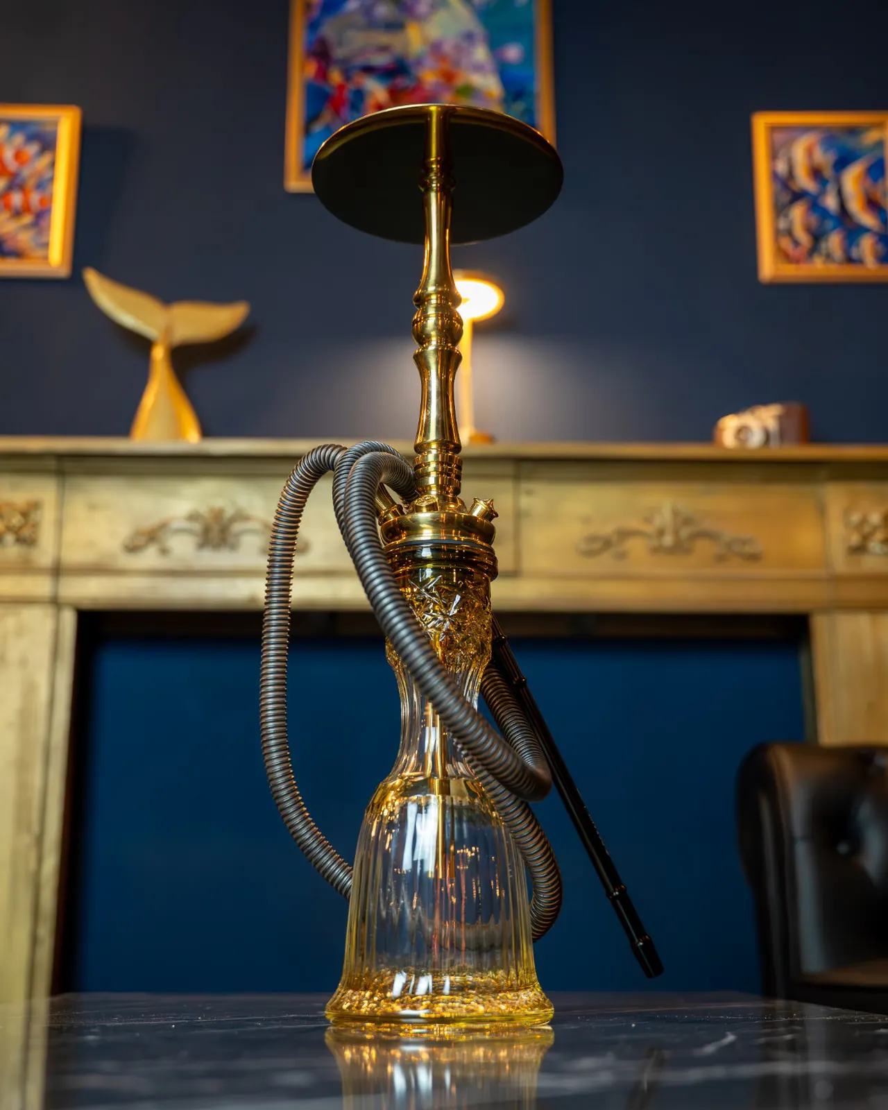 Shisha dorada con base de cristal sobre una mesa de mármol, delante de la chimenea dorada